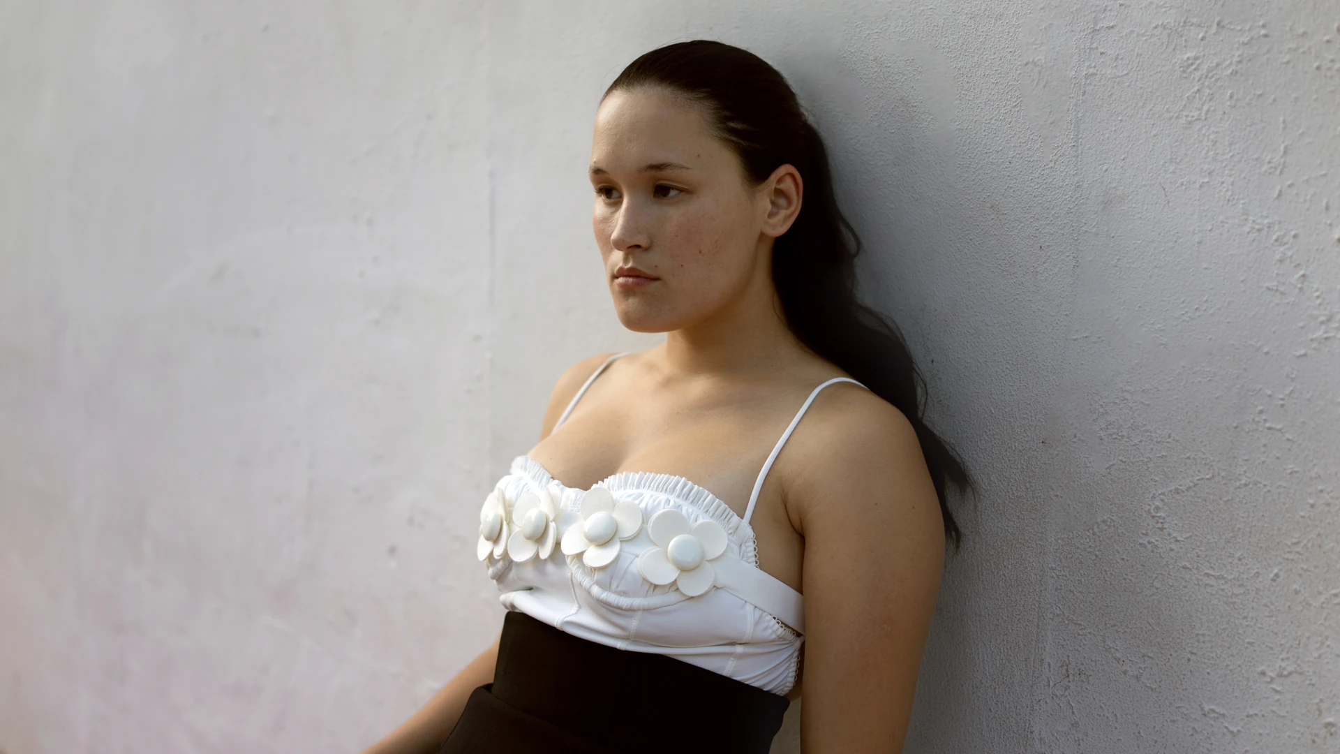 Woman leaning on a grey wall in a white flower bustier